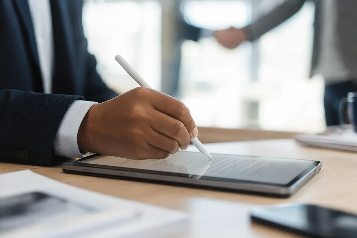 Signature d’un contrat d’assurance auto sur une tablette numérique, poignée de main en arrière-plan
